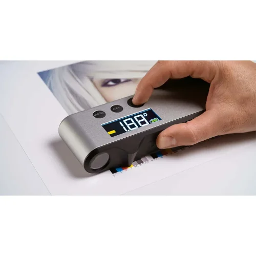 TECHKON DENS podczas pracy na wydruku z paskiem kontrolnym CMYK. Zdjęcie pokazuje praktyczne użycie densytometru do kontroli jakości druku, szybkiego pomiaru gęstości i oceny stabilności koloru.