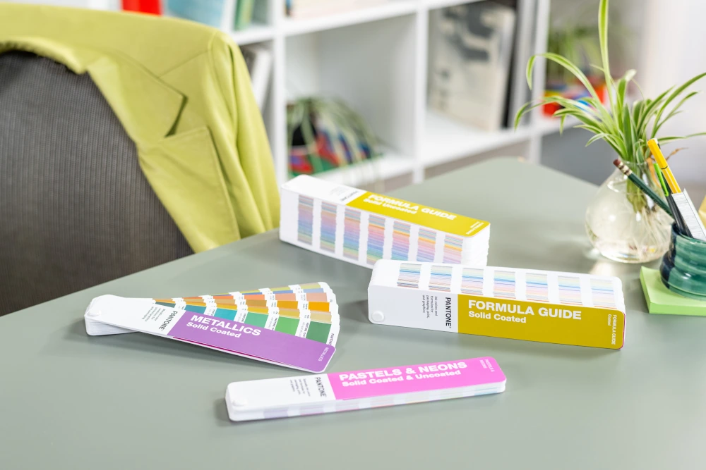 Pantone Solid Guide Set używany na biurku projektowym z Formula Guide, Metallics oraz Pastels and Neons